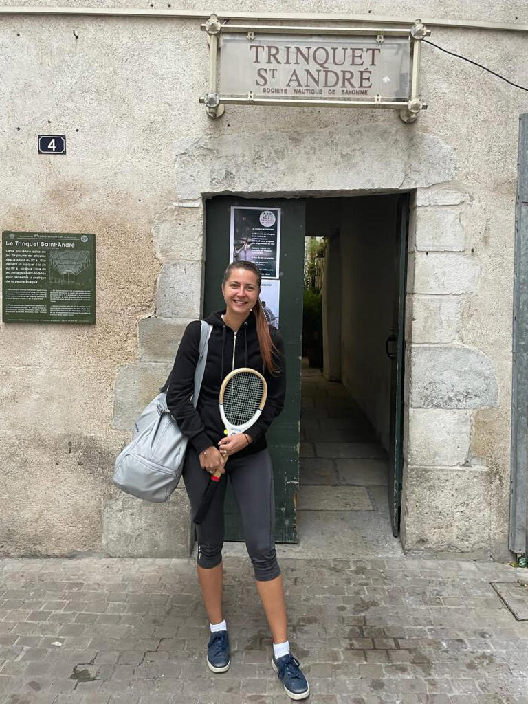 Irina Dulbish holding a racket in front of a trinquet St. Andre court entrance